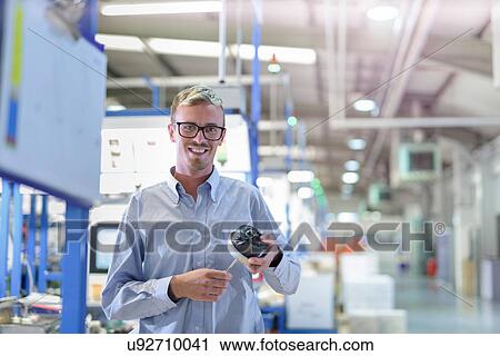 Stock Image - Portrait of engineer holding 3D printed exhaust valve actuator in factory. Fotosearch