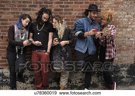 Stock Photo - Portrait of friends using smartphones against brick wall. Fotosearch