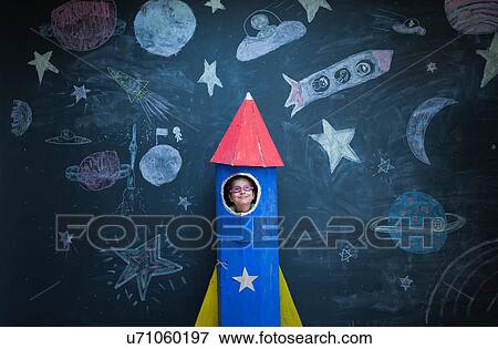 Stock Photo - Portrait of girl in handmade space rocket in front of space themed chalk drawings. Fotosearch