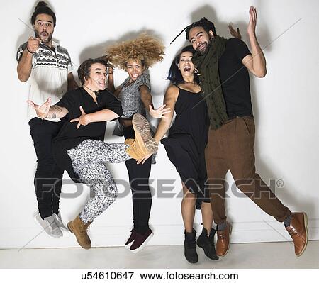 Stock Photo - Portrait of group of happy friends against white wall jumping. Fotosearch