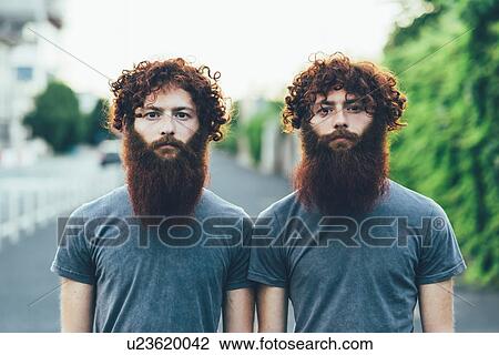 Stock Image - Portrait of identical adult male twins with red hair and beards on sidewalk. Fotosearch