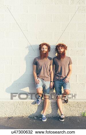 Stock Image - Portrait of identical adult male twins with red hair and beards against white wall. Fotosearch