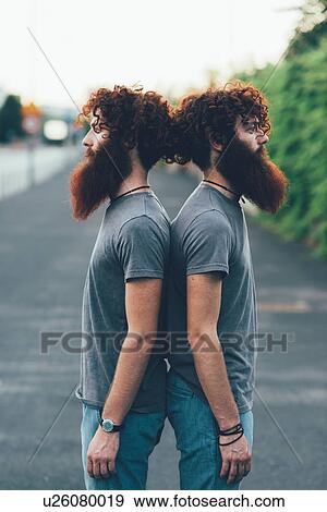 Stock Photo - Portrait of identical adult male twins with red hair and beards back to back on sidewalk. Fotosearch