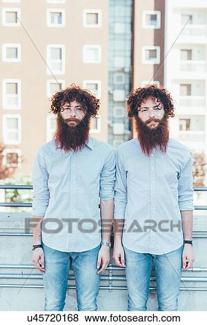 Stock Photo - Portrait of identical male hipster twins standing on apartment roof terrace. Fotosearch