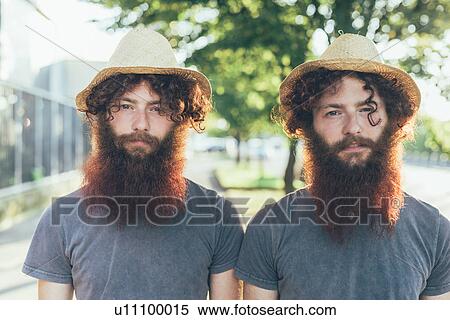 Stock Photography - Portrait of identical male hipster twins wearing straw hats on sidewalk. Fotosearch