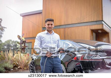 Portrait of man charging electric car View Large Photo Image Stock Photo - Portrait of man charging electric car. Fotosearch