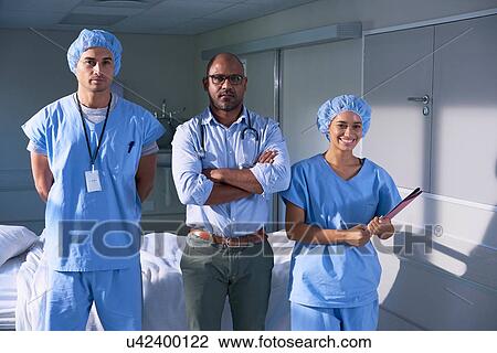 Stock Image - Portrait of mature male doctor and two medics on hospital ward. Fotosearch