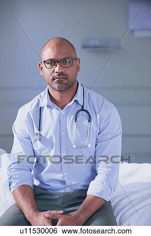 Portrait of mature male doctor sitting on hospital bed View Large Photo Image Stock Photograph - Portrait of mature male doctor sitting on hospital bed. Fotosearch