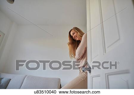 Stock Image - Portrait of mid adult woman leaning against living room door. Fotosearch