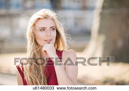 Stock Image - Portrait of pretty young woman with long blond hair in park. Fotosearch