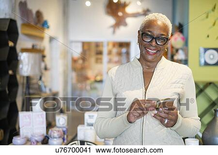 Stock Image - Portrait of woman holding mobile phone in shop. Fotosearch