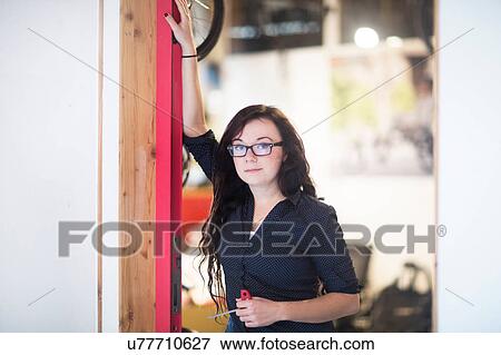 Stock Photo - Portrait of woman leaning against door frame looking at camera. Fotosearch