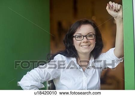 Stock Image - Portrait of woman leaning against wall looking at camera smiling. Fotosearch