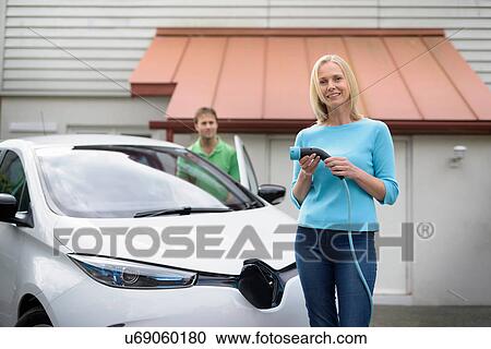 Portrait of woman with electric car, holding charging plug View Large Photo Image Stock Image - Portrait of woman with electric car, holding charging plug. Fotosearch