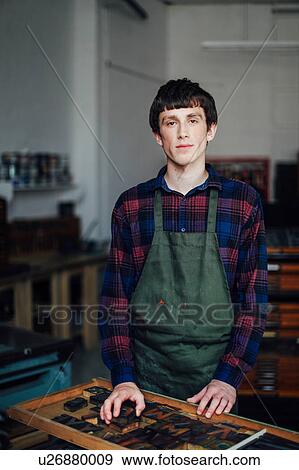 Stock Photo - Portrait of young craftsman next to tray of letterpress letters in print workshop. Fotosearch