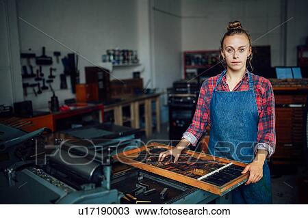 Stock Image - Portrait of young craftswoman next to tray of letterpress letters in print workshop. Fotosearch