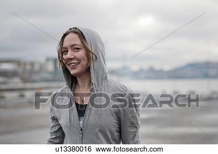 Stock Photograph - Portrait of young female runner wearing hoody on windy dockside. Fotosearch