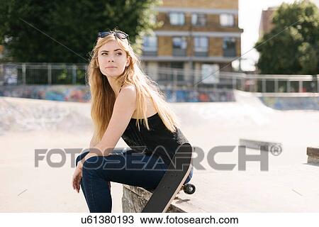 Stock Image - Portrait of young female skateboarder sitting in skatepark. Fotosearch