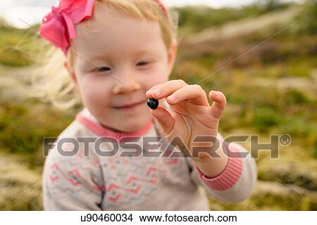 Picture - Portrait of young girl outdoors, holding blueberry. Fotosearch