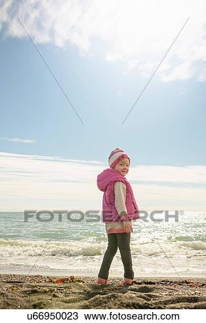 Stock Image - Portrait of young girl standing beside sea, looking over shoulder. Fotosearch