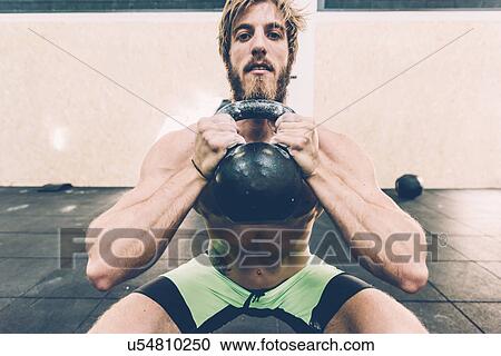 Stock Image - Portrait of young male cross trainer training with kettlebell in gym. Fotosearch