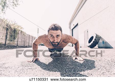 Stock Image - Portrait of young male cross trainer doing push-ups outside gym. Fotosearch