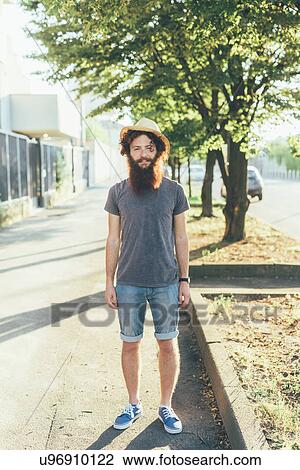 Stock Image - Portrait of young male hipster wearing straw hat on sidewalk. Fotosearch