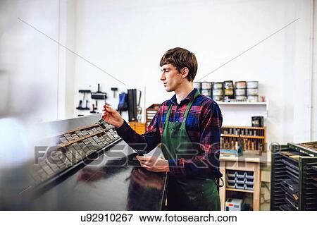 Stock Photo - Profile shot of young craftsman looking at metal letterpress spacing in a book arts workshop. Fotosearch