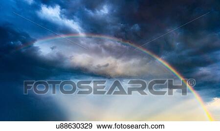 Rainbow against dramatic sky at sunset View Large Photo Image Stock Photo - Rainbow against dramatic sky at sunset. Fotosearch