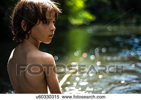 Stock Photography - Rear view of boy by water looking away over shoulder. Fotosearch