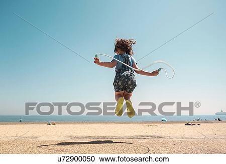 Stock Image - Rear view of girl in mid air skipping on beach, Southwold, Suffolk, UK. Fotosearch