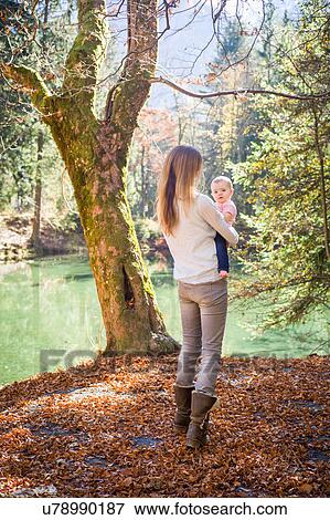 Stock Photo - Rear view of mother and baby girl in forest by water. Fotosearch