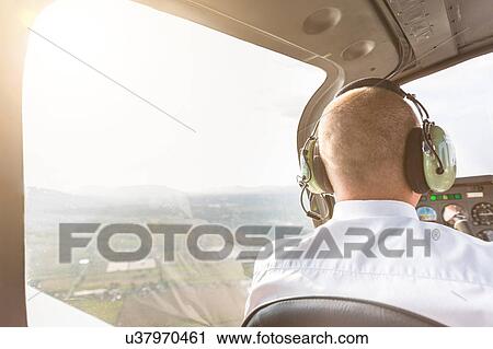 Stock Image - Rear view of pilot in cockpit of aircraft, in flight. Fotosearch