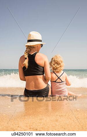 Rear view of woman and daughter sitting on beach at waters edge, Altea, Alicante Province, Spain View Large Photo Image Stock Image - Rear view of woman and daughter sitting on beach at waters edge, Altea, Alicante Province, Spain. Fotosearch