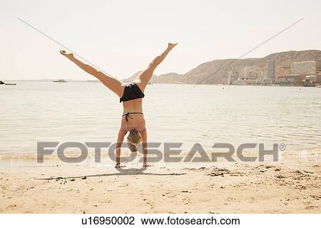 Stock Image - Rear view of woman in bikini cartwheeling on beach, Alicante, Spain. Fotosearch