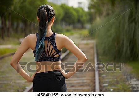 Stock Photography - Rear view of woman on railway track, hands on hips. Fotosearch