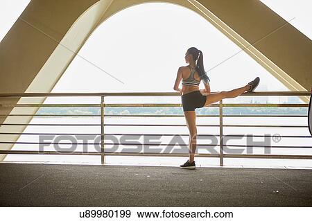 Stock Photo - Rear view of woman with leg raised on railing stretching. Fotosearch