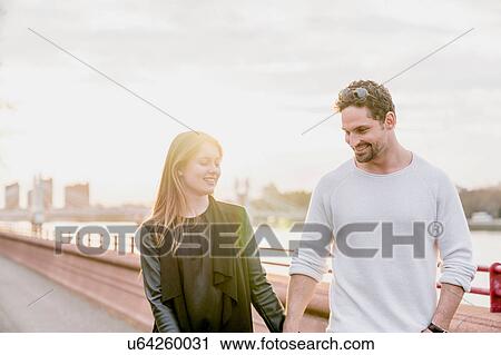 Stock Image - Romantic couple strolling on waterfront at sunset, Battersea Park, London, UK. Fotosearch