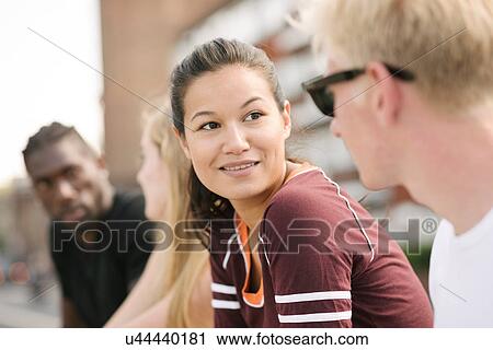 Stock Image - Row of four male and female friends chatting in city skatepark. Fotosearch
