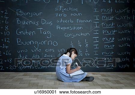 Stock Image - Schoolgirl sitting studying in front of large chalkboard with schoolwork chalked on it. Fotosearch