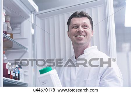 Stock Photo - Scientist holding bottle of chemical removed from cabinet. Fotosearch