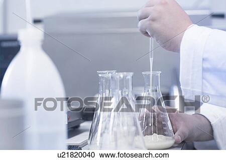 Stock Image - Scientist pipetting sample into beaker in laboratory. Fotosearch