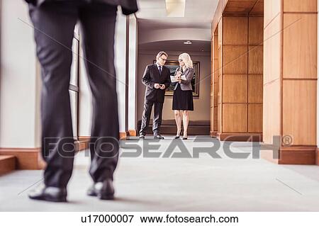 Stock Photo - Senior businessman and woman talking in office corridor. Fotosearch