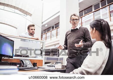 Stock Photo - Senior businessman explaining to businesswoman at office desk. Fotosearch