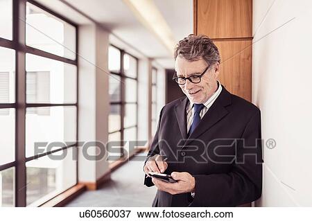 Senior businessman in office corridor using smartphone touchscreen View Large Photo Image Stock Photo - Senior businessman in office corridor using smartphone touchscreen. Fotosearch