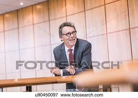 Stock Photo - Senior businessman leaning against office balcony. Fotosearch