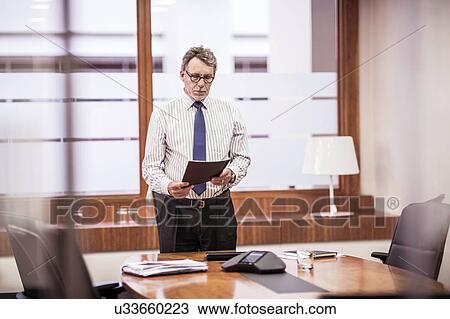 Senior businessman reading paperwork at boardroom table View Large Photo Image Stock Image - Senior businessman reading paperwork at boardroom table. Fotosearch
