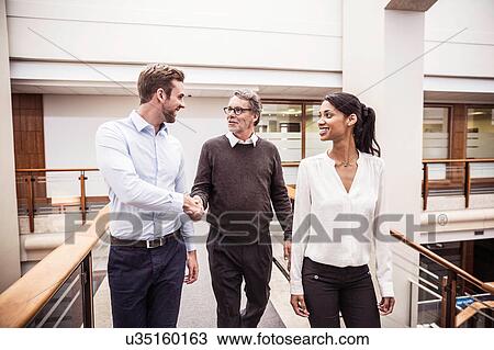 Stock Image - Senior businessman shaking hands with client on office walkway. Fotosearch