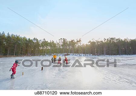 Stock Image - Senior couple and grandchildren practicing ice skating slalom on frozen lake, Gavle, Sweden. Fotosearch