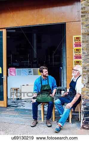 Senior craftsman drinking coffee and chatting to young man outside workshop View Large Photo Image Stock Photo - Senior craftsman drinking coffee and chatting to young man outside workshop. Fotosearch